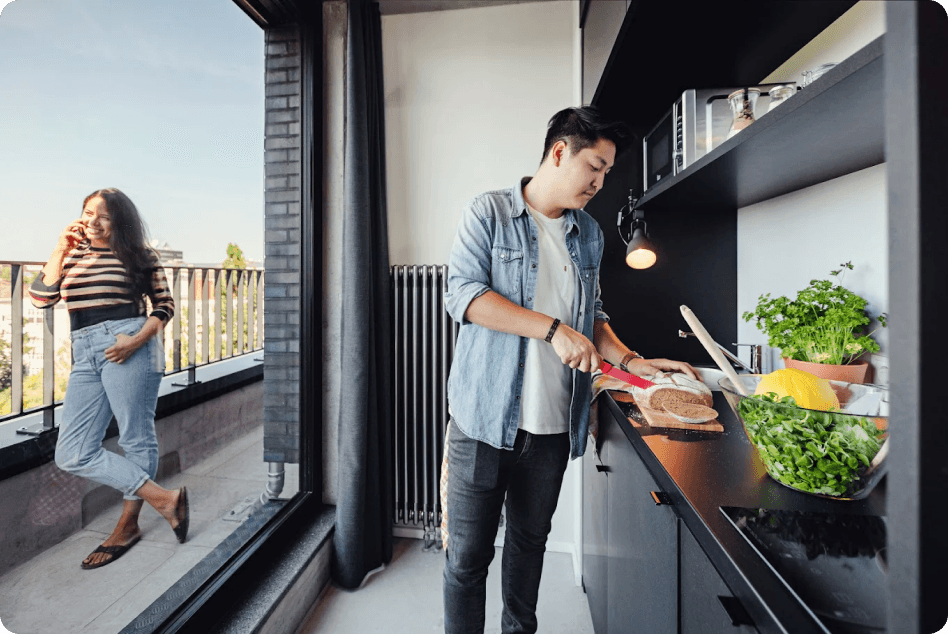 Resident cooking in a Neon Wood apartment kitchen with a city balcony view